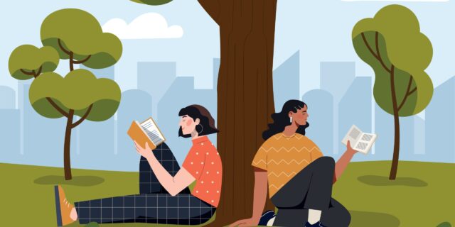 A pair of women sit against a tree while reading books.